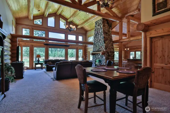 Stunning great room with soaring ceilings, floor-to-ceiling stone fireplace, and expansive wall of windows capturing the surrounding natural setting.