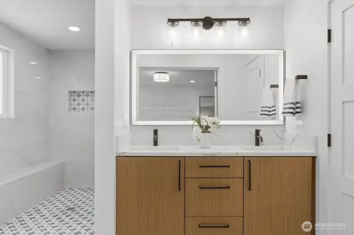 The primary suite features a gorgeous resort-style bathroom showcasing designer 30" x 60" porcelain tile, an elegant backlit mirror, and a dreamy oversized walk-in shower.