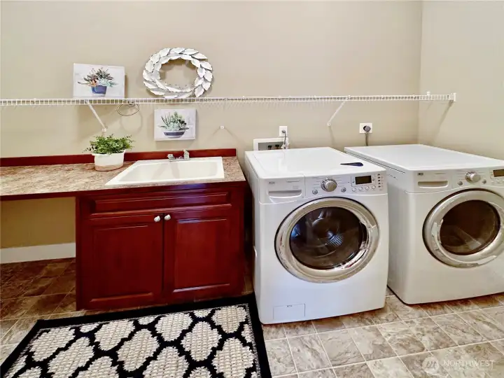 Big laundry room with sink and storage cabinets and shelves.