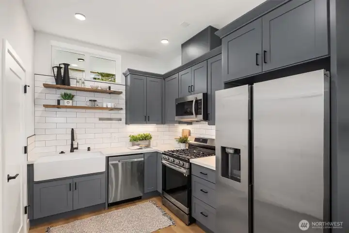 Quartz counters, drop-in sink, gas range and stainless appliances with a side by side fridge.