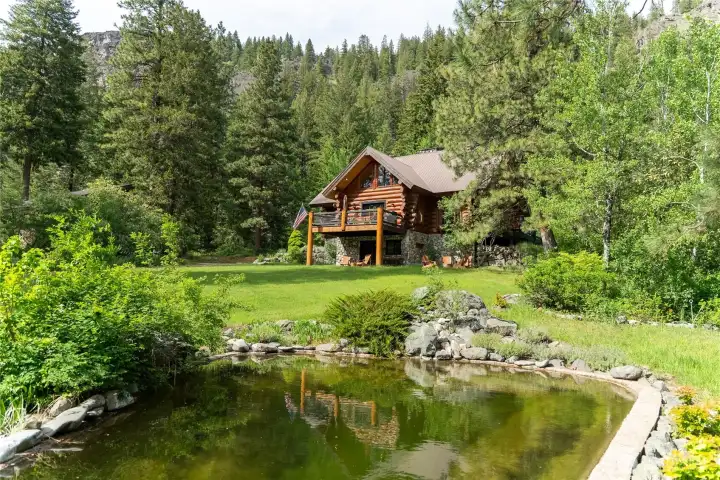 Peaceful mountain setting with landscaped pond, open lawn, and custom lodge-style home tucked into the trees below dramatic rock outcroppings. Designed to embrace the natural beauty, privacy, and year-round recreation of the Methow Valley.