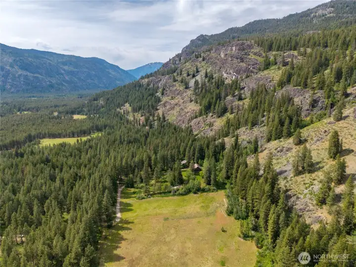 Sweeping aerial view looking north across the private meadow and surrounding wilderness landscape, with the sounds of Thiese Creek cascading and meandering through the property below dramatic rock cliffs of adjoining National Forest land. A peaceful mountain setting defined by privacy, open space, near by community trails and adjoins National Forest Land.
