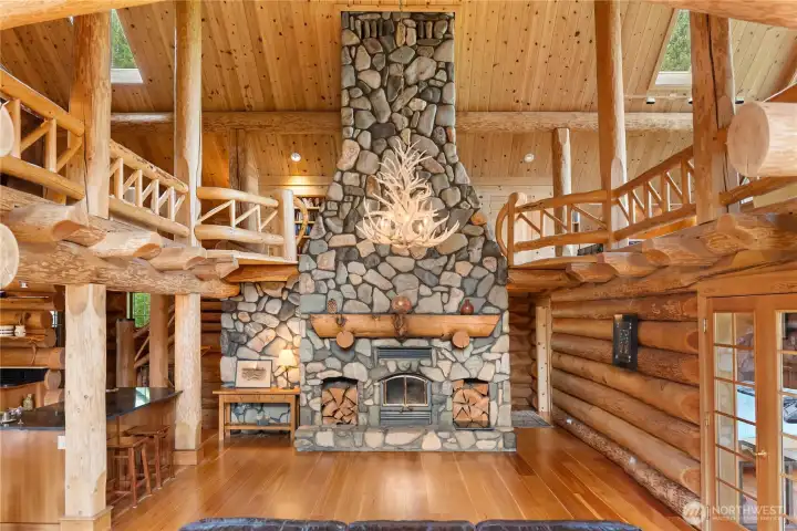 The dramatic floor-to-ceiling hand-stacked river rock fireplace anchors the great room, creating a warm and unforgettable gathering space at the heart of the home. Massive timber beams, handcrafted log details, and the surrounding loft complete the classic lodge-style atmosphere.