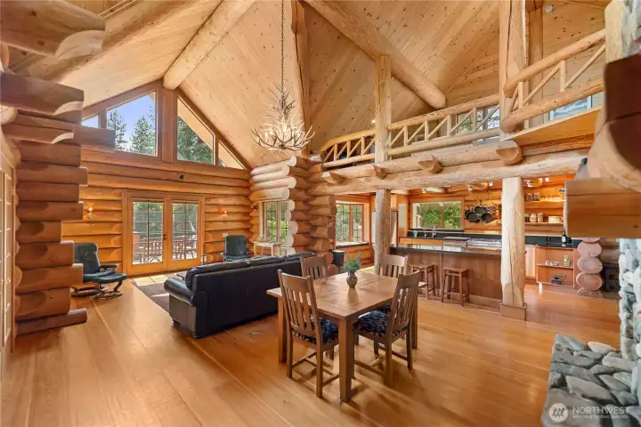 Soaring timber ceilings, massive handcrafted logs, and walls of windows create a dramatic great room filled with natural light and authentic log character. The open design, surrounding loft, and seamless connection between living, dining, and kitchen spaces were crafted for gathering, entertaining, and relaxed mountain living.