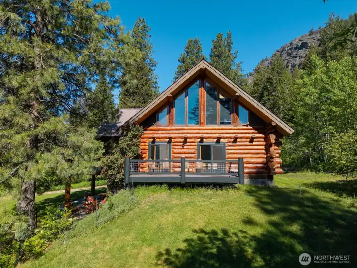 Southern view of the custom lodge-style home overlooking open lawn, gardens, and surrounding mountain terrain, with expansive decks and outdoor living spaces designed to embrace the peaceful Methow setting.