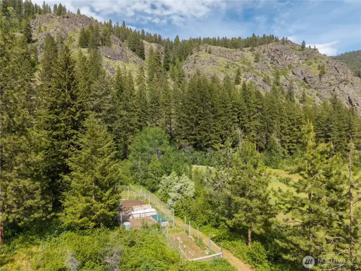 Fenced gardens with raised beds ready for fresh greens, herbs, garlic, berries and seasonal harvests beneath dramatic National Forest cliffs and surrounding wilderness.