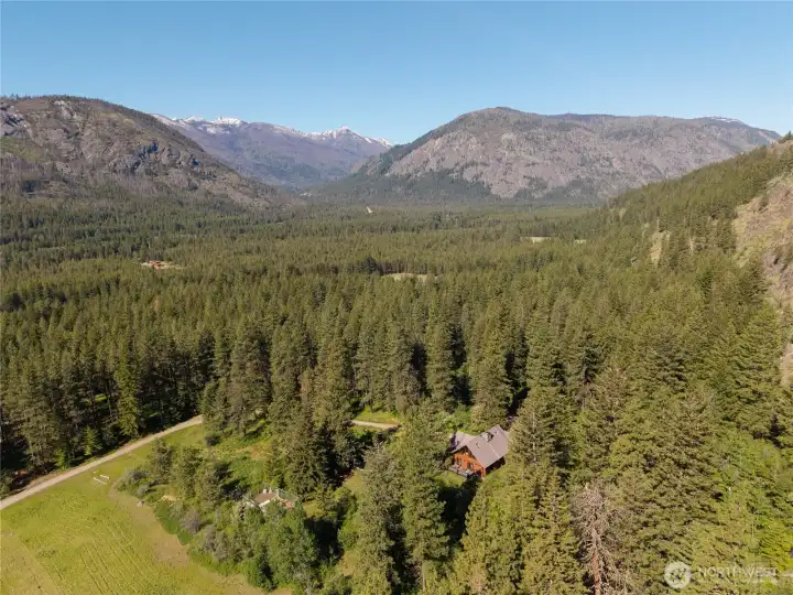 Looking northwest toward the North Cascades, with sweeping views of surrounding mountains, forested hillsides, open meadows, and the Highway corridor winding through the valley below.
