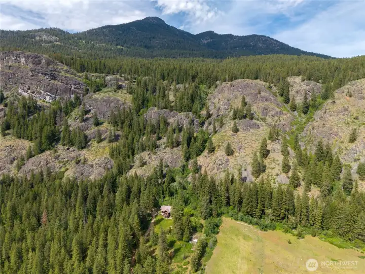 Blue skies and dramatic mountain scenery surround this private retreat, with Goat Peak rising prominently at 7,100 feet in the backdrop. Thiese Creek waterfall is tucked into the rugged hillside above, with the creek meandering along the eastern portion of the property below towering evergreens and open meadowlands.