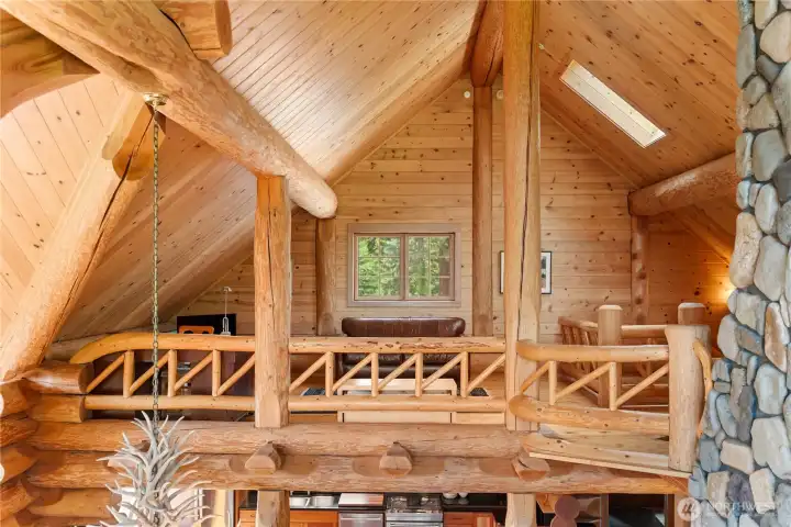 Expansive upper-level loft overlooks the great room below, showcasing massive log beams, handcrafted wood railings, soaring ceilings, and endless natural wood detail throughout. Flexible gathering spaces create the perfect setting for reading, games, conversation, home office use, a cozy sleeping nook, or quiet relaxation in this true mountain lodge retreat.