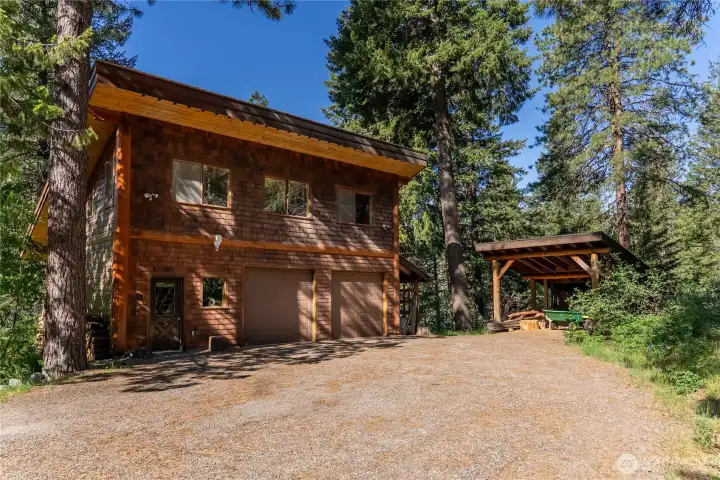 Cedar-sided detached two-car garage with gravel approach, covered wood storage area, and stairs leading to a fully finished upper-level flex space ideal for a bunk room, guest overflow, studio, recreation room, creative workspace, or private retreat, with power connected and excellent separation from the main home.