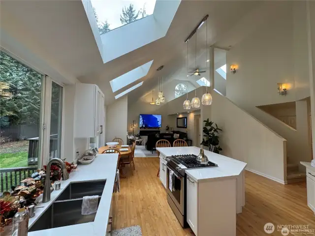 Open concept kitchen and family room featuring vaulted ceilings and three new extra large skylights and a bright loft overlooking the space that includes two additional new skylights - creating a spacious, airy, and connected living area perfect for both everyday life and entertaining.