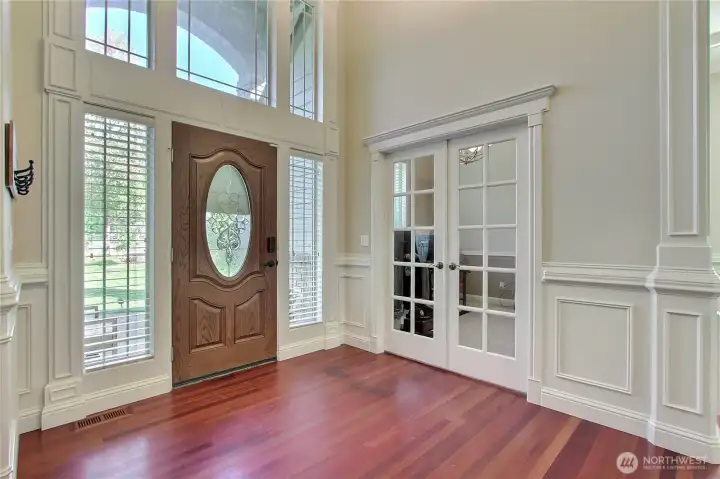 As you step through the front door, you're greeted by soaring 18-foot ceilings that create a dramatic and unforgettable first impression. Rich Brazilian cherry wood floors guide you into the heart of the home, setting a warm and luxurious tone from the moment you enter. To your left, classic French doors open to a flexible space perfect for a home office or formal sitting room. Straight ahead, a grand double-sided staircase sweeps upward, offering both functionality and a stunning architectural focal point.