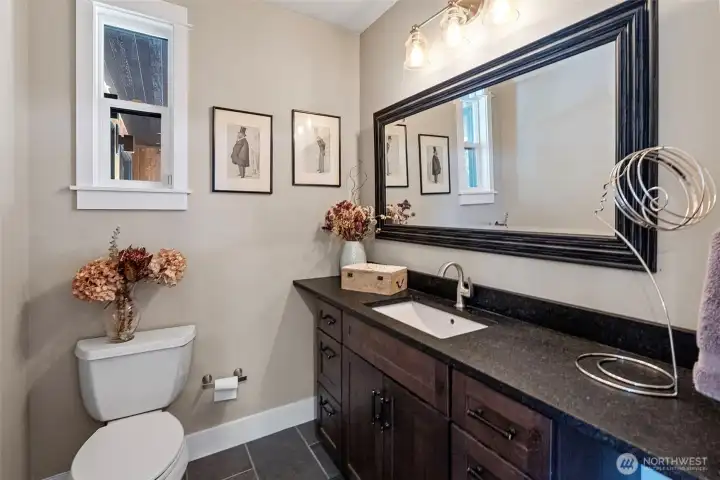 A powder room is positioned just off the kitchen and enjoys a beautiful vanity and tile flooring.