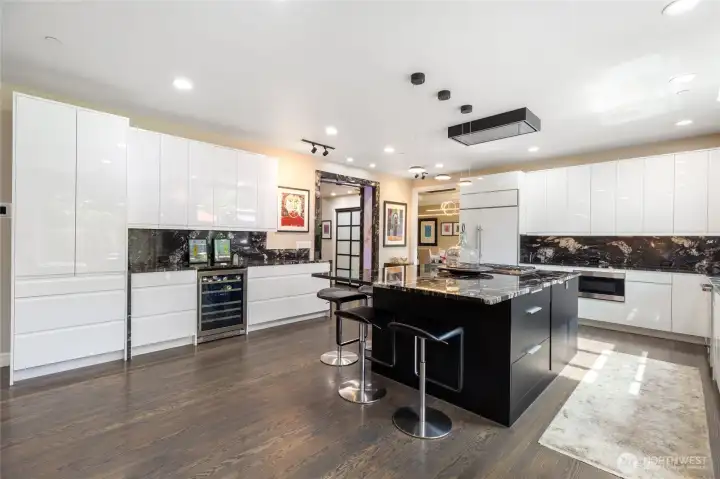 Expansive kitchen with modern custom cabinetry, integrated wine storage, Wolf and Sub-Zero appliances, striking stone backsplash, and designer lighting—blending style and functionality throughout