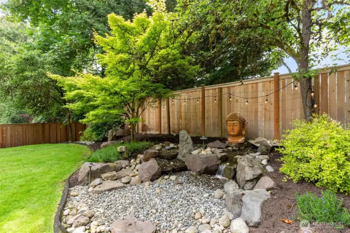 Serene landscaped backyard with tranquil water feature, mature greenery, and a private, peaceful setting.
