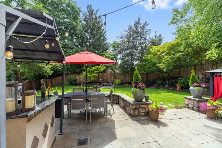 Resort-style backyard oasis featuring an expansive stone patio,  outdoor bar, and dining area with café lighting—perfect for entertaining.