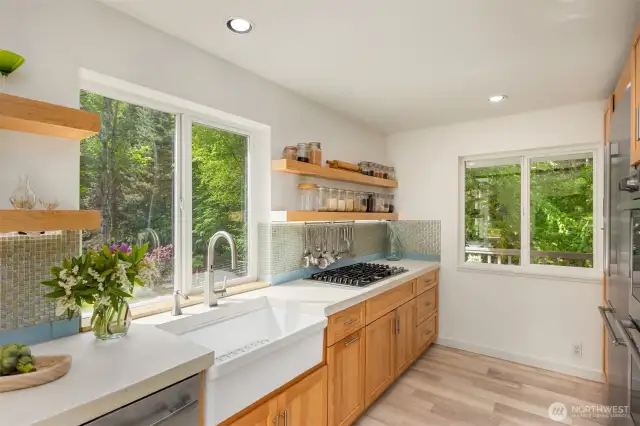 The deep porcelain sink overlooks the lush yard and features a touchless faucet. Gorgeous and substantial maple open shelving displays your prettiest or most-used items, and conceals undermount lighting. The kitchen designer thought of everything!