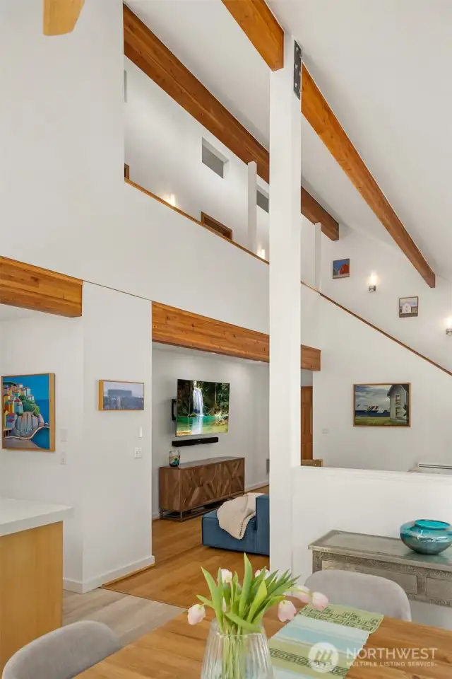 I love this view of the architecturally stunning great room as seen from the dining table. Exposed wood beams provide warmth and interest, drawing the eye to soaring ceilings and the artful second-story with interior clerestories.