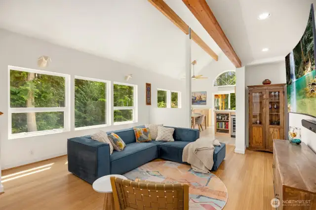 The great room is a showcase of the home, graced by a wall of windows across the living room (near) and dining room (far), then sliders to the sunny deck with a covered grilling station off the kitchen.