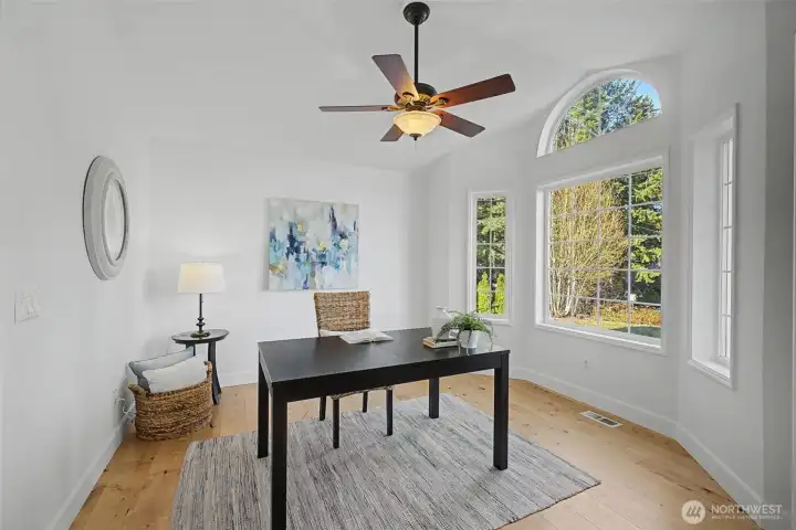 This serene, sunlit room works beautifully as a home office or formal dining space. An elegant arched transom window and tall side windows fill the room with natural light, while warm wood floors and soft neutral finishes create a calm, inviting atmosphere. A ceiling fan adds year-round comfort, making this an ideal setting for remote work, creative projects or intimate gatherings.