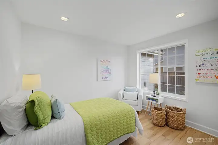This inviting guest bedroom is located toward the front of the home and features warm wood floors, recessed lighting and a large window that brings in soft natural light. Clean lines and neutral finishes create a calm, comfortable atmosphere, making this an ideal space for guests, a home office or a flexible hobby or exercise room.