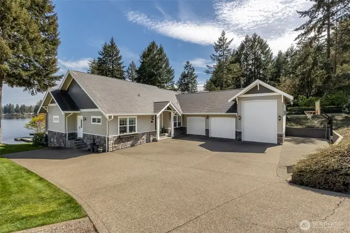 The wide driveway isn’t just for show, it actually works. Pull right up next to the mudroom door for easy unloads, park a boat or trailer along the side, and still have room for guests to come and go without the usual shuffle. The three-car garage includes an RV-height door, and yes, you still catch a glimpse of the water as you come down the drive. The exterior brings it home with stone accents grounding the base and Hardiplank siding above for durability that looks good long-term.