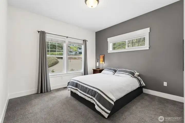 This main-level bedroom overlooks the driveway and keeps things bright without giving up privacy thanks to that high-set panoramic window. It lets the light in while keeping furniture placement flexible, no awkward bed-against-the-window situations here. The gray accent wall adds just enough depth to keep it from feeling flat, and the plush carpet keeps it soft underfoot. With 9-foot ceilings, the room has a little extra breathing space that makes it feel more open than your average secondary bedroom.