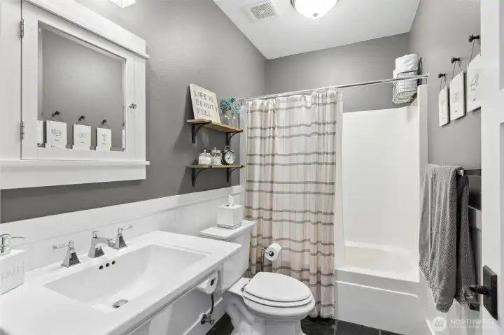 Right where you want it, this full bath sits conveniently next to the lower-level sleeping spaces, making it feel like a true guest or extended living setup. The pedestal sink keeps things classic and clean, with a medicine cabinet above for those everyday essentials. A full tub and shower combo adds flexibility, whether it’s quick mornings or longer stays. Beadboard wainscoting brings in a little texture and charm, while the 9-foot ceilings keep the space from feeling tight.