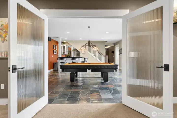 The slate tile floors set the tone, durable, a little moody, and ready for actual use, not just looking pretty. The pool table is already in place and yes, it stays, so game night is officially handled. Those reeded glass French doors add just enough separation without killing the vibe, leading into an 18’ x 9½’ bonus space that’s basically a wildcard. Lounge, office, overflow guests, hobby zone, you decide. It’s the kind of setup that doesn’t box you in, it gives you options.