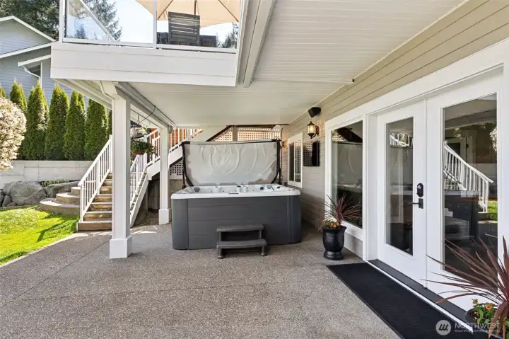 Glass French doors open onto an aggregate concrete patio that feels clean, durable, and ready for real use. Tucked under the upper deck, the covered hot tub area is basically year-round permission to relax, rain included. And the layout? Smart. Stairs sit right next to the spa, giving you a quick, easy path up to the main deck, living areas, and primary suite without doing a full house lap. It’s seamless, it’s practical, and it’s exactly how you want indoor-outdoor living to work.