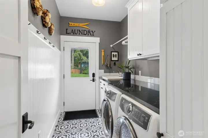 This is one of those spaces that quietly makes life easier. Coming straight in from the driveway, it’s set up perfectly for real life, muddy shoes, wet gear, all handled right here without tracking it through the house. The utility sink is ready for cleanup duty, and the folding counter over the washer and dryer keeps things efficient without sacrificing style. Beadboard wainscoting and matching shaker cabinetry add that tailored, finished look, while the Moroccan-inspired tile floor brings in just enough personality to keep it interesting. Soft gray walls above tie everything together, giving the room a clean, collected feel.