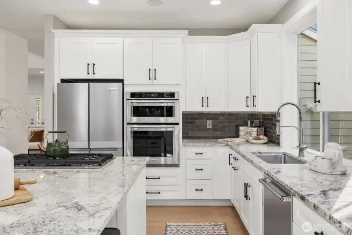 this designer kitchen features sleek granite slab surfaces, full-height subway tile backsplash, and a premium KitchenAid appliance suite