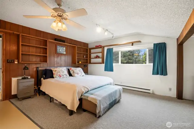 The primary bedroom is very spacious and looks out to the front lawn. There are built-in shelves at the wood-paneled wall.