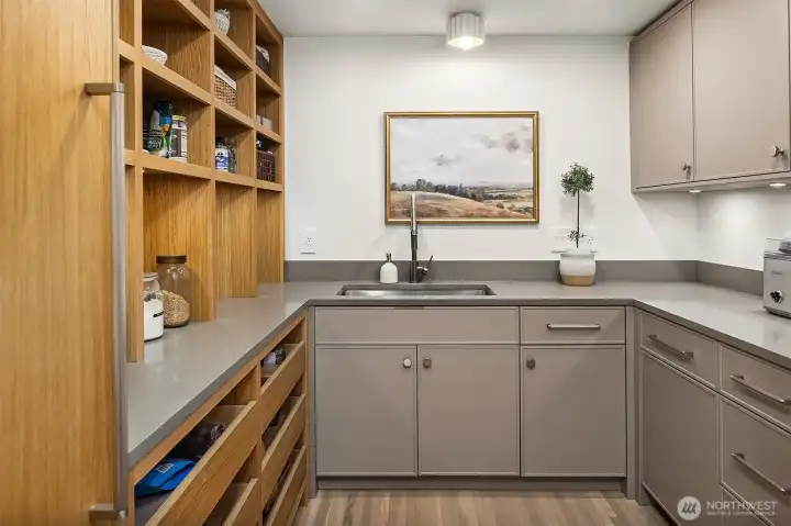 Walk-in pantry with sink and extra dishwasher. Paneled freezer and open white oak shelving with light. Walk-in pantry with sink and extra dishwasher. Paneled freezer and open white oak shelving with light.