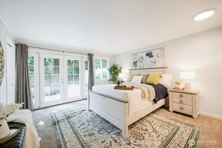 Welcome to the roomy primary suite!  French doors open to the patio and has its own bath. Filled with warmth and light. Queen size bed with two night stands and still so much room to move around.