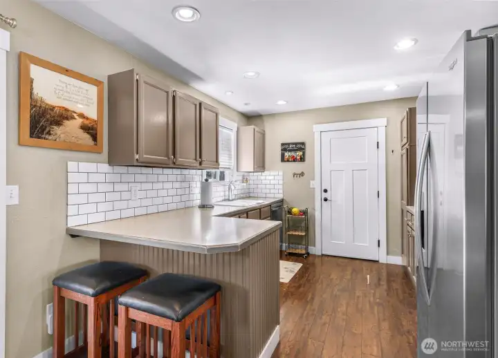Kitchen features a breakfast bar, subway tile backsplash & stainless steel appliances. Door to garage is shown at center Kitchen features a breakfast bar, subway tile backsplash & stainless steel appliances. Door to garage is shown at center