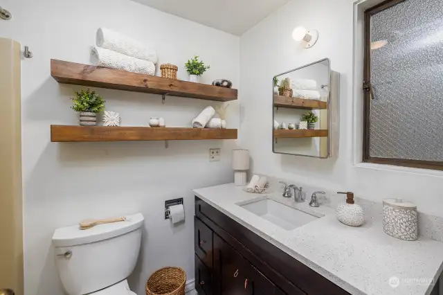 Cute bathroom with floating wood shelving and updated cabinetry.