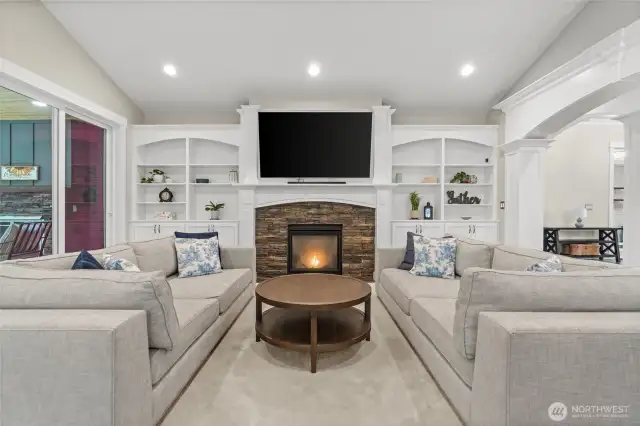 Stunning built-in shelves and cabinets flank the gas fireplace, creating a beautiful focal point in the great room. They perfectly complement the wood-wrapped pillars, detailed millwork, and graceful arched doorways, delivering a cohesive and refined aesthetic throughout the space.
