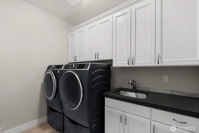 A large laundry room includes upper and lower cabinets, washer and dryer and a utility sink.