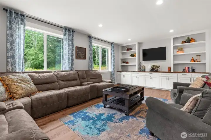 The spacious flex room features custom built-in cabinetry, open shelving, and large windows overlooking the surrounding greenery, offering space for media, recreation, or additional living needs.