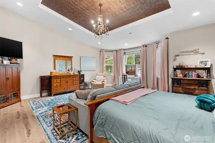 The spacious primary suite features a decorative tray ceiling with chandelier, a comfortable sitting area, and direct access to the adjoining en suite bathroom.