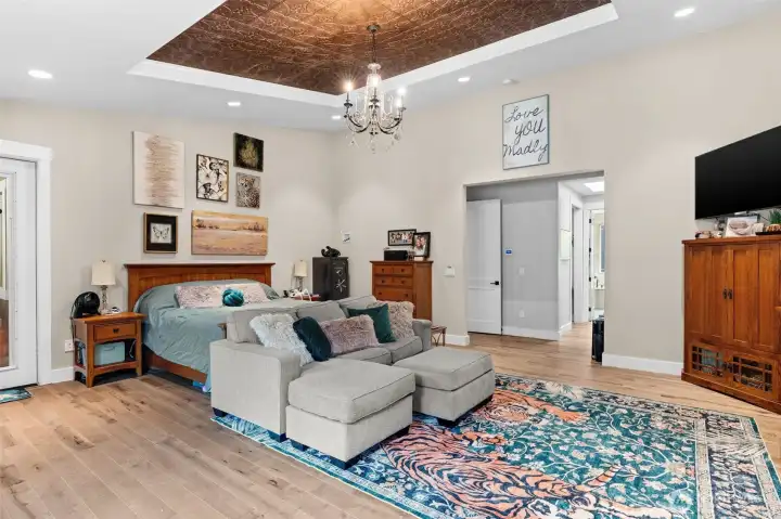 The spacious primary suite features a decorative tray ceiling with chandelier, a comfortable sitting area, and direct access to the adjoining en suite bathroom.
