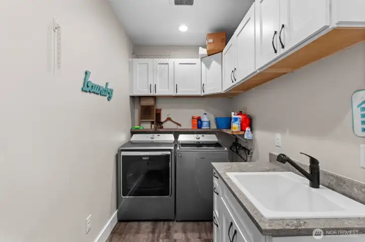 Laundry room features upper cabinetry, a utility sink, and countertop workspace for added functionality.
