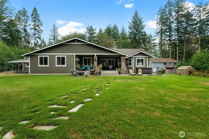 Backyard view showcases the covered patio, landscaped lawn, detached shop, and separate upper-level ADU.