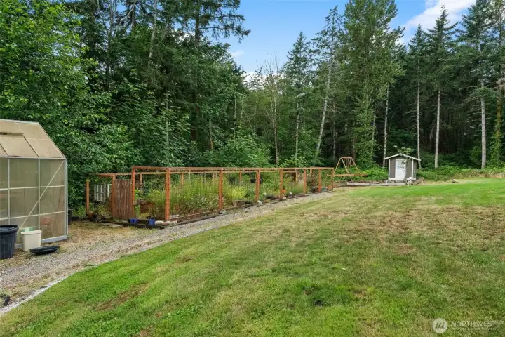 Thoughtfully arranged outdoor space with raised garden beds, greenhouse, storage shed, and open lawn.