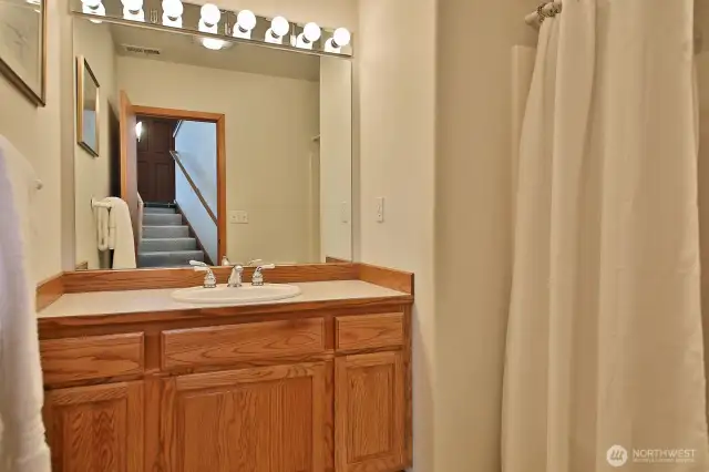 Lower level Full Bath is located at the base of the stairs across from the Laundry Room. You can see the stairs to the entry way in the mirror.