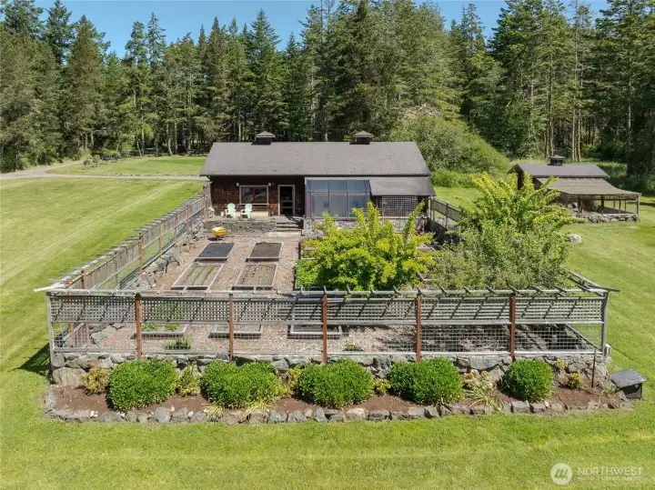 Large shop/garage with attached greenhouse overlooks the fenced garden with fruit trees.  Elegant chicken house to the right.