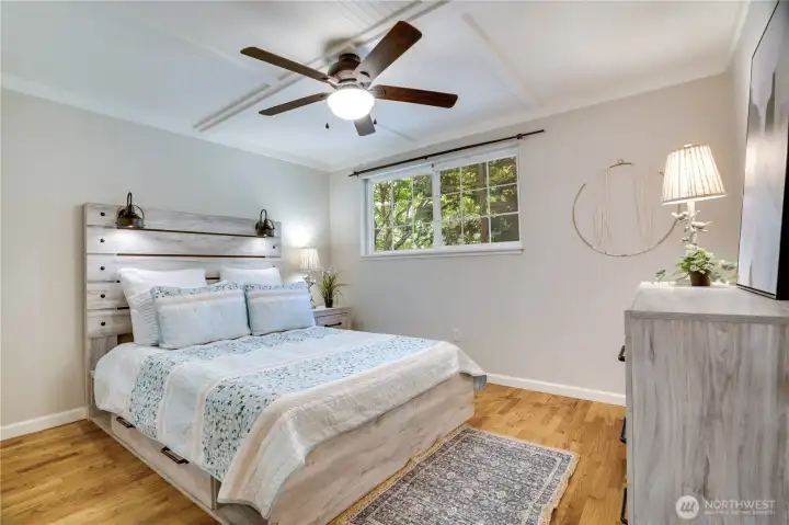 Warm hardwood floors, shiplap ceilings, and natural light create a comfortable retreat in the primary bedroom. A ceiling fan adds year-round comfort. Warm hardwood floors, shiplap ceilings, and natural light create a comfortable retreat in the primary bedroom. A ceiling fan adds year-round comfort.
