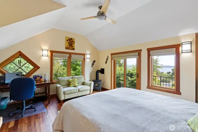 Large primary bedroom with balcony, view, love seat, propane stove, ceiling fan, and office space.