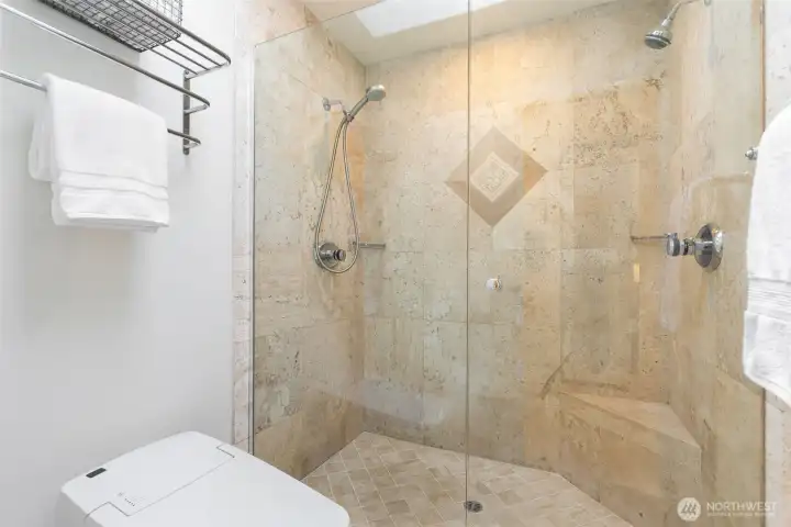 Stylish travertine tile, frameless glass, and heated bidet toilet